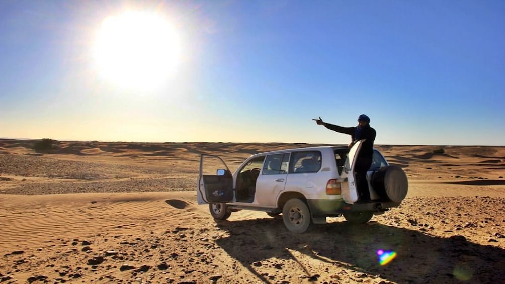 Man stands on back of Jeep and points toward Hurghada desert