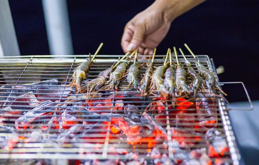 Hand turns small squid on sticks over coals 