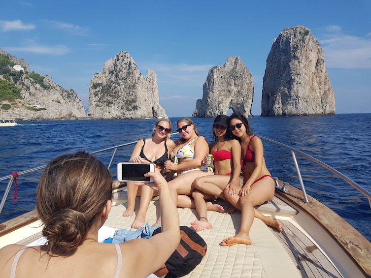 Show item 1 of 10. Friends pose for picture on deck of boat in front of Faraglioni rock stacks