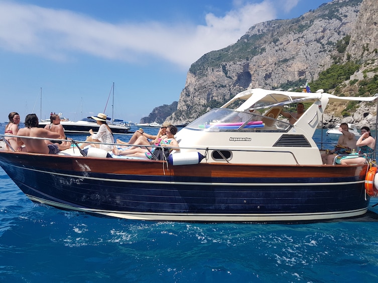 Show item 4 of 10. Tourists on a boat in the bright blue waters of Capri, Italy