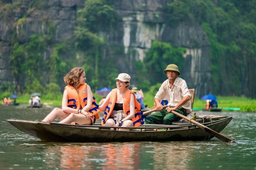 Tourists and guide sit in rowboat in Tam Coc Wharf