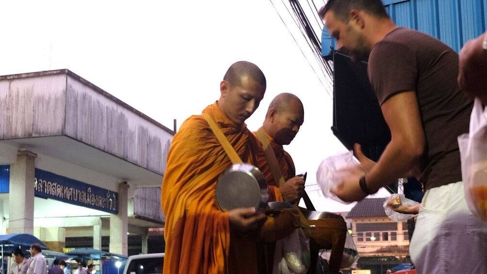 Man gives alms to Buddhist monk in Thailand