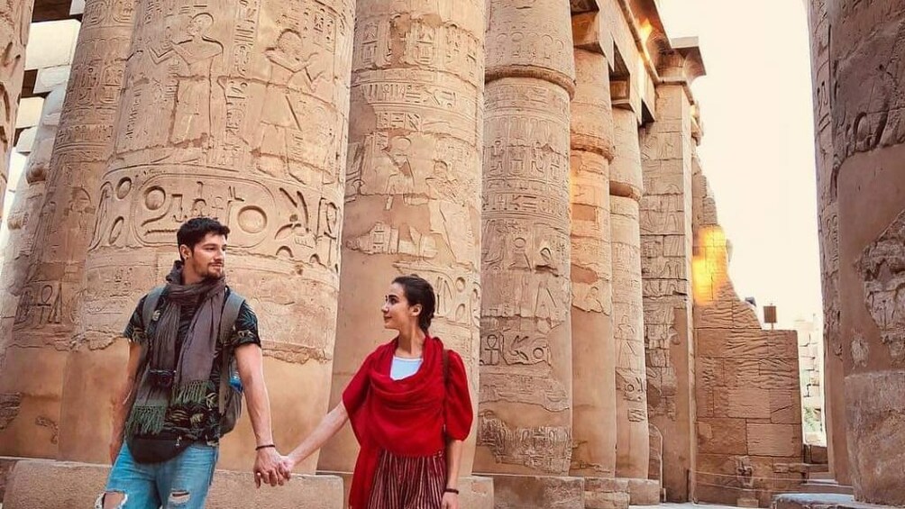 Couple hold hands in front of large, carved pillars at Egyptian temple