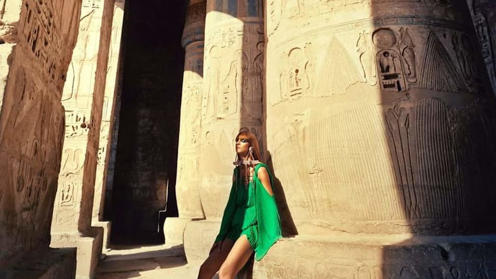 Woman poses in front of large, carved pillar at an Egyptian temple