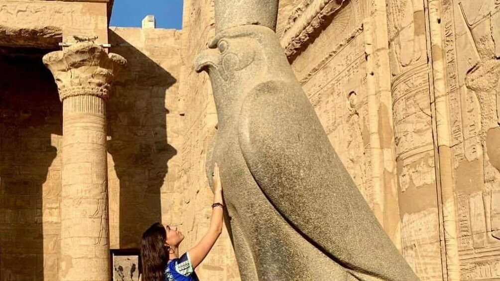 Woman puts hand on large Horus statue at the Temple of Horus at Edfu