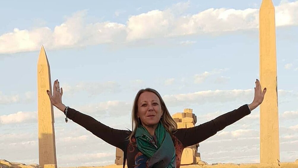 Woman poses with arms outstretched as if leaning against two obelisks