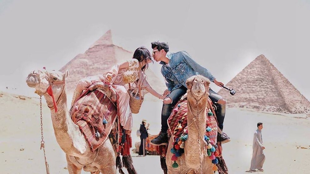 Couple kiss while sitting on two camels in front of the Pyramids of Giza