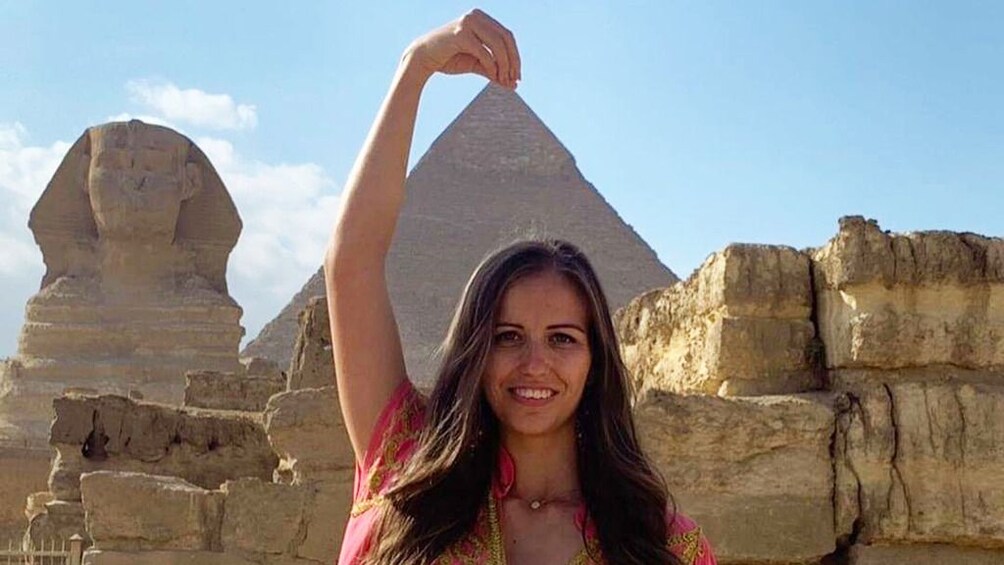 Woman stretches her arm above her head to make it look like she is touching the top of the Great Pyramid of Giza