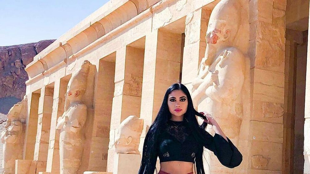 Woman poses in front of large statues of Egyptian temple