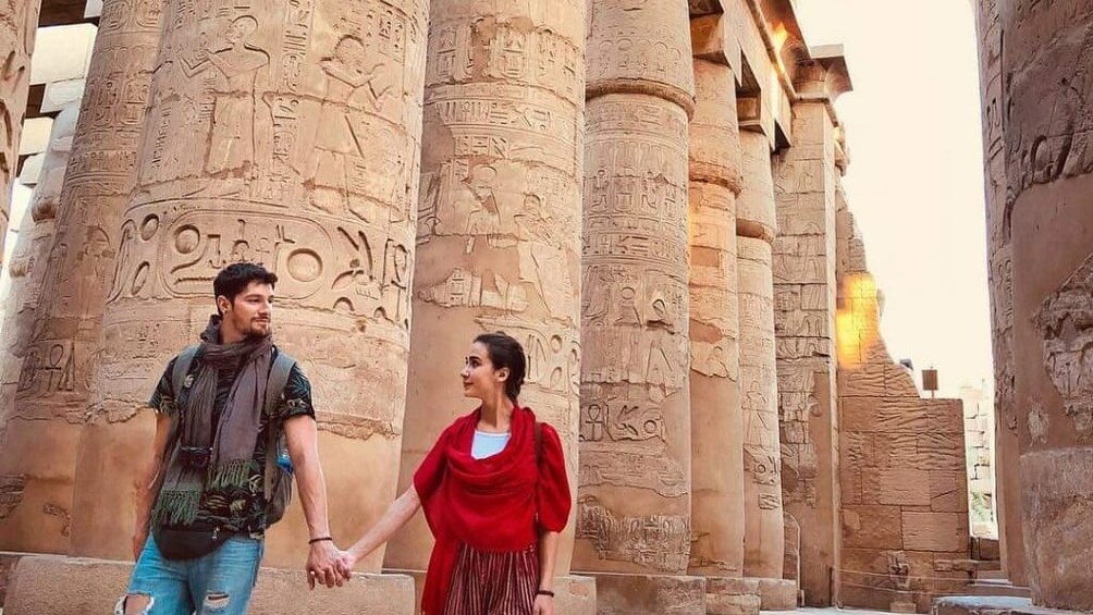 Couple hold hands in front of large carved Egyptian columns