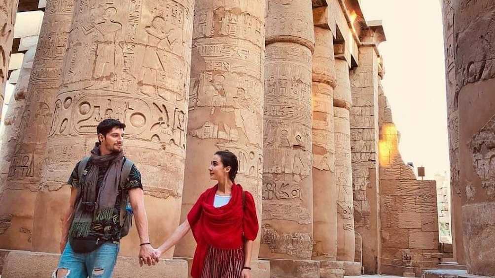 Couple hold hands in front of large columns with hieroglyphics