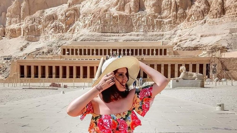 Woman with large hat poses in front of the Mortuary Temple of Hatshepsut in Egypt 