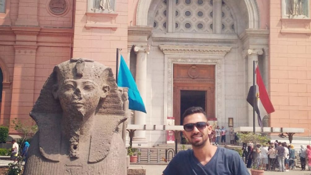 Man poses next to small sphynx statue in front of Egyptian Antiquities Museum
