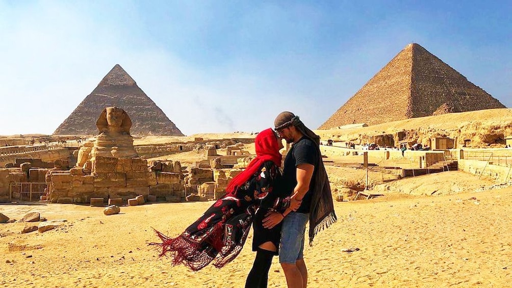 Couple stands together in front of the Pyramids and Sphynx of Giza, Egypt