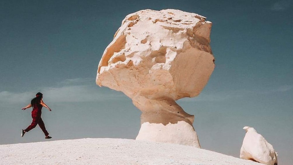 Woman runs towards large boulder in White Desert of Egypt