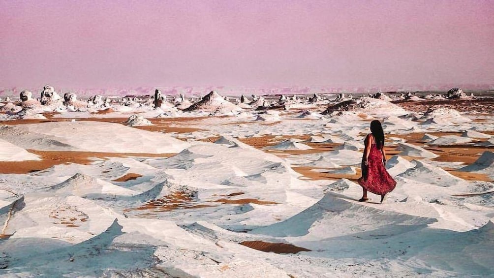 Woman walks through White Desert in Egypt at sunset