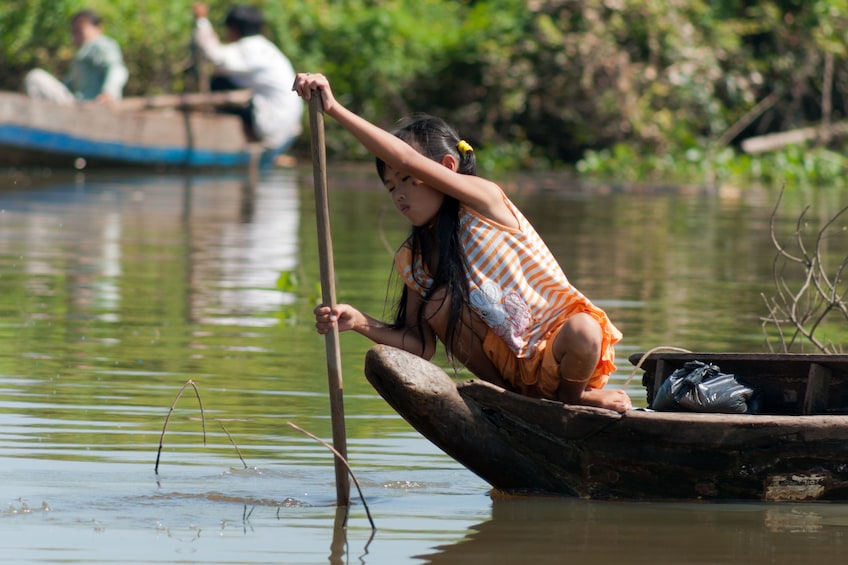 Young woman rows small boat in Tonle Sap Lake in Cambodia