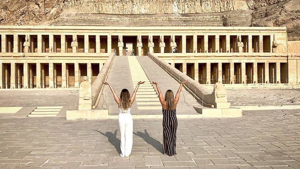 Two women pose with hands in the air in front of Mortuary Temple of Hatshepsut
