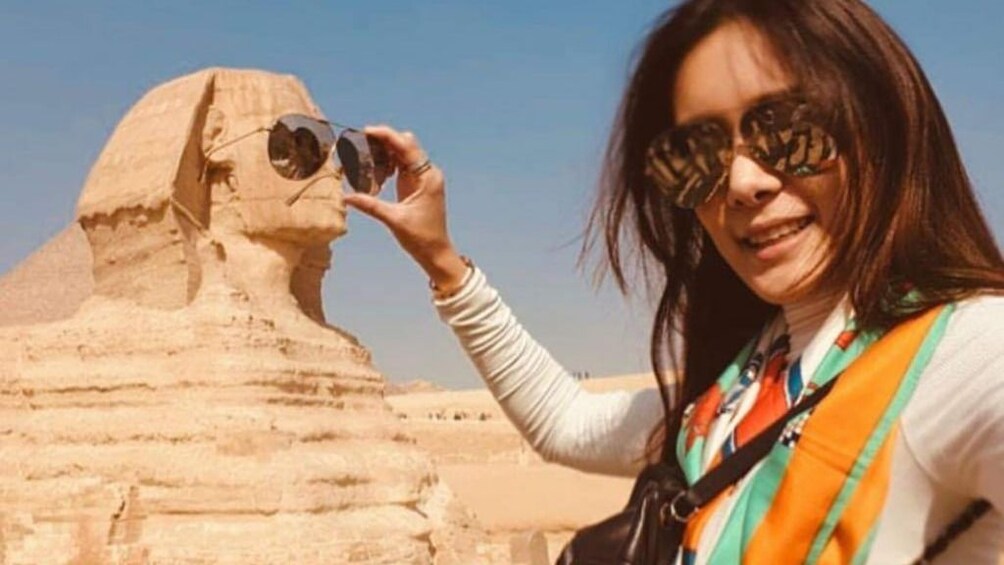 Woman holds pair of sunglasses in front of Sphinx of Giza