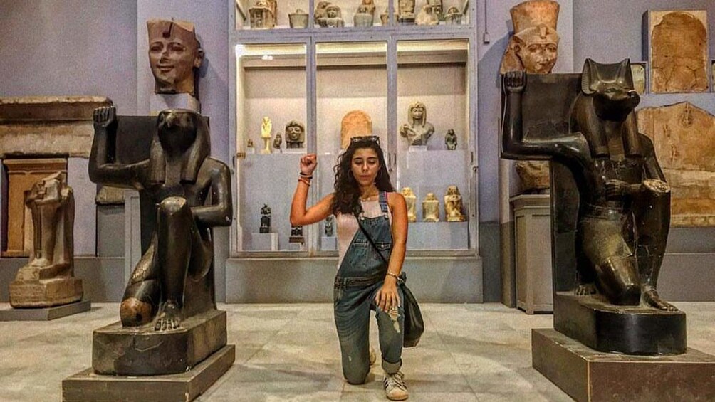 Woman kneels between two kneeling ram statues in Egyptian Museum