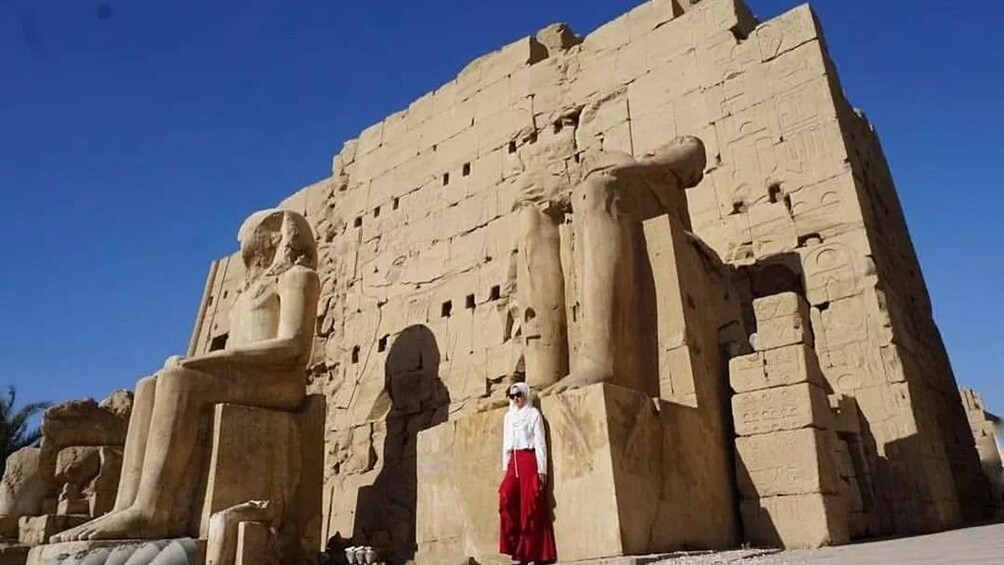 Woman stands in front large Pharaoh statues in Egypt