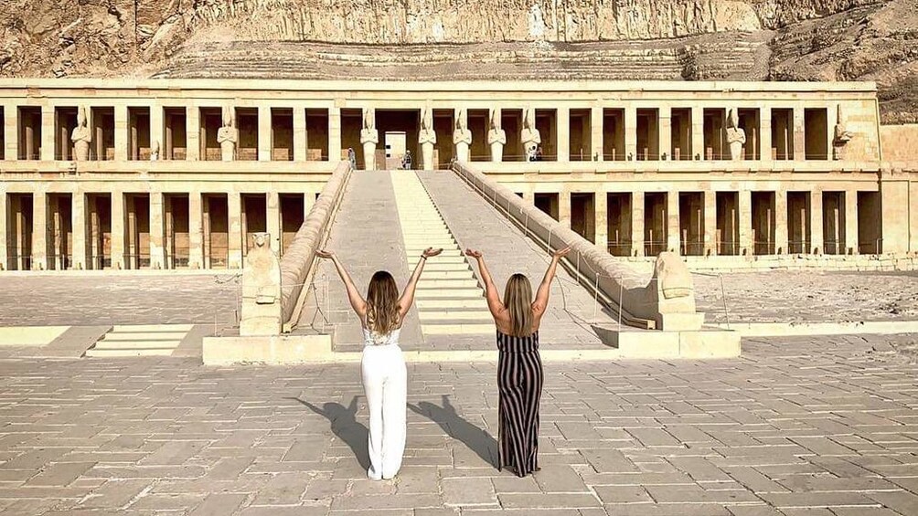 Two girls pose with arms outstretched in front of the Mortuary Temple of Hatshepsut