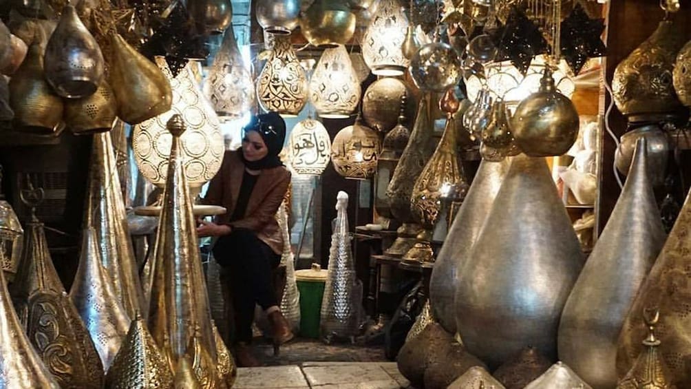 Woman sits in Egyptian market surrounded by carved metal lanterns
