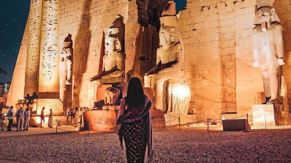 Woman walks towards Egyptian temple lit up at night
