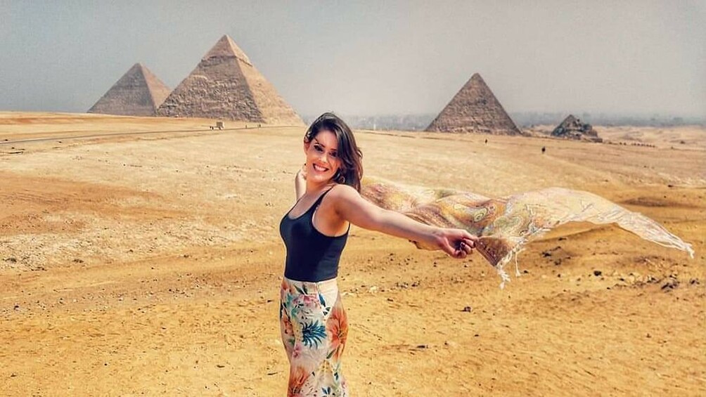 Woman poses holding scarf with the Pyramids of Giza in the distance