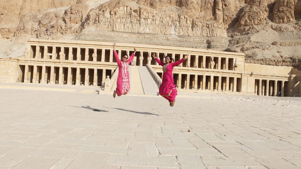 Two women jump and pose in front of the Temple Mortuary of Hatshepsut