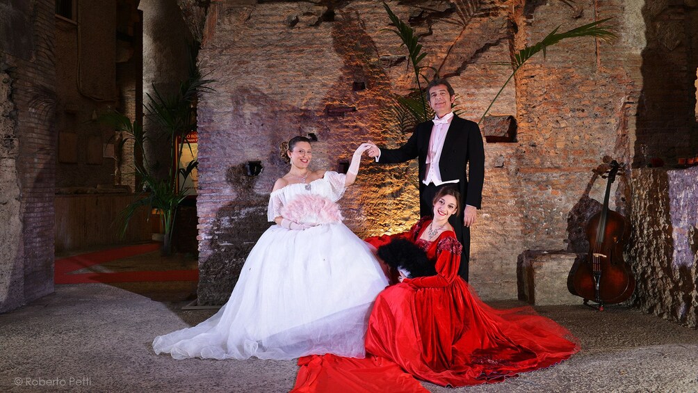 Three opera performers pose in front of brick wall at Roman Opera