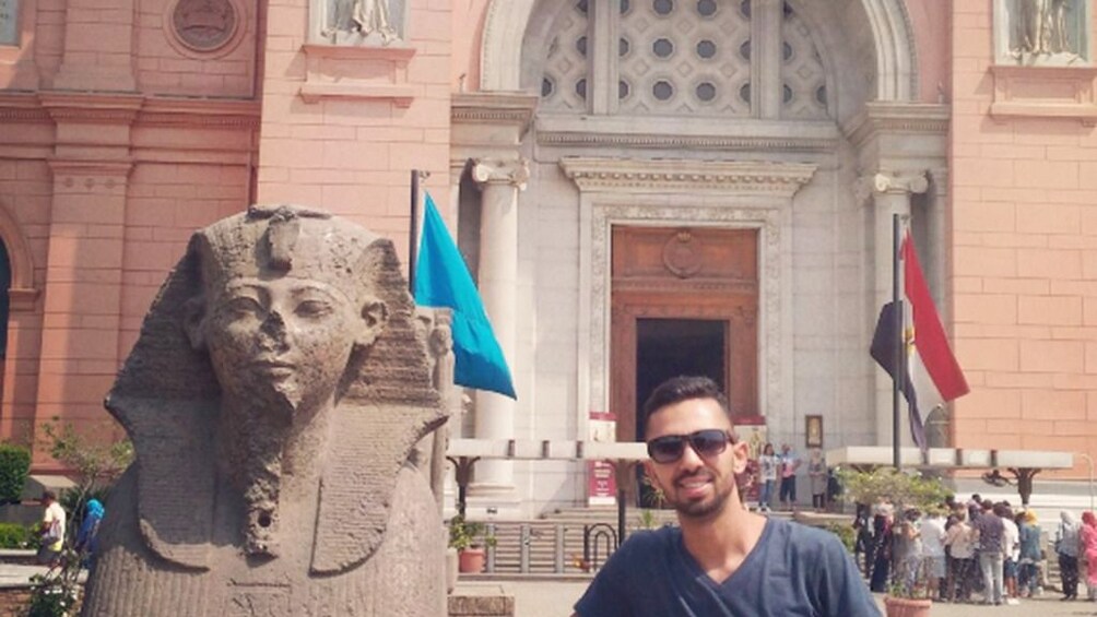 Man poses next to small Sphinx in front of Egyptian Museum in Cairo, Egypt