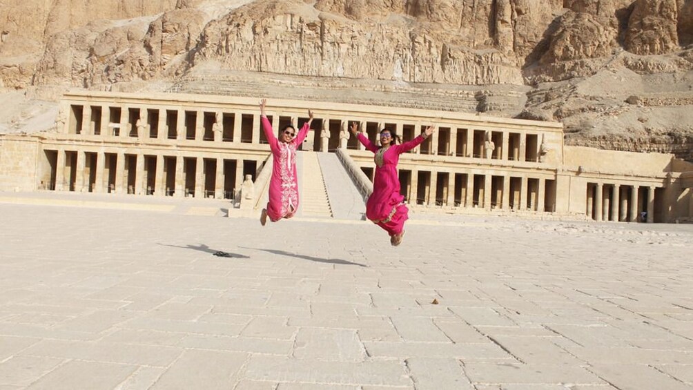 Two women in red jump in front of Mortuary Temple of Hatshepsut