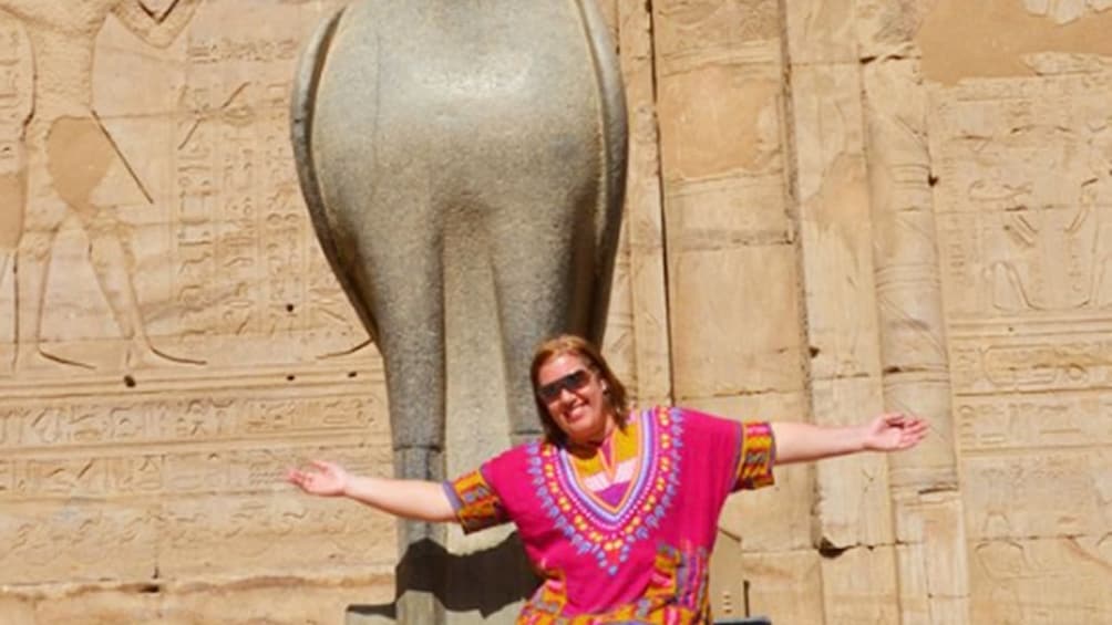 Woman in colorful top poses with statue of Horus at the Temple of Horus at Edfu