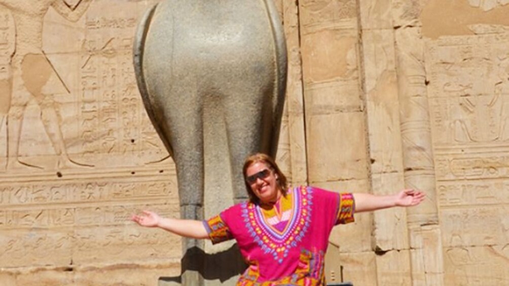 Show item 3 of 7. Woman in colorful top poses with statue of Horus at the Temple of Horus at Edfu