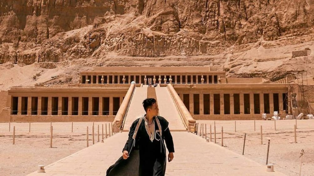 Man in robe poses in front of Mortuary Temple of Hatshepsut