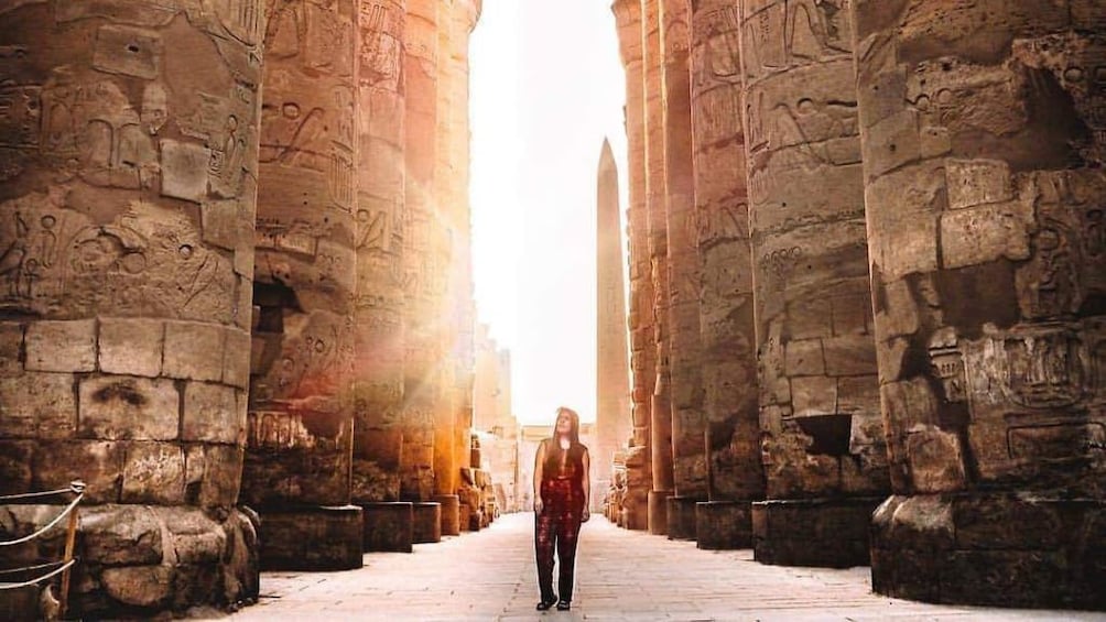 Woman stands among large Egyptian columns at sunset