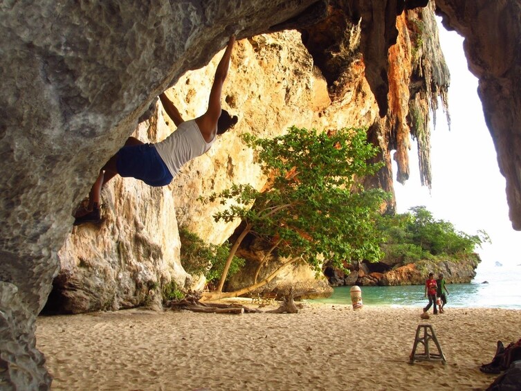 Woman rock climbing as guests walk by at Railay Beach in Krabi