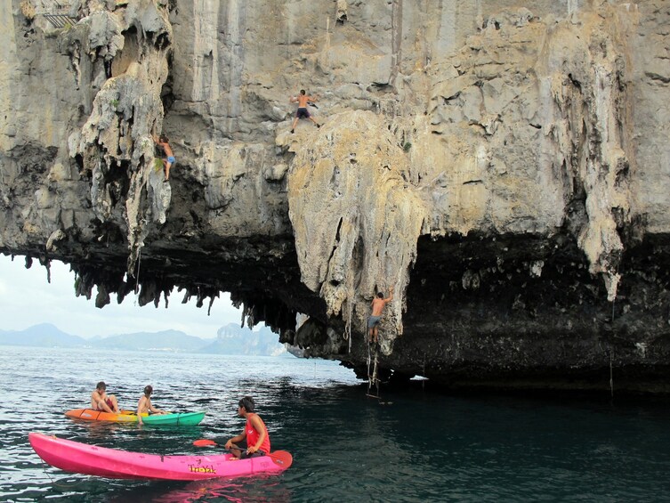 Group rock climbing right on Railay Beach in Krabi while some guests are in the water kayaking 