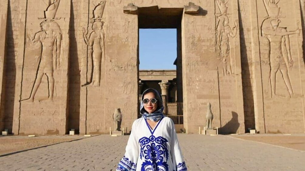 Woman in blue and white dress poses in front of the Temple of Horus at Edfu