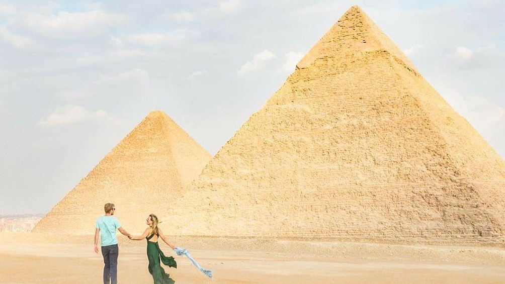 Couple hold hands in front of the Pyramids of Giza 