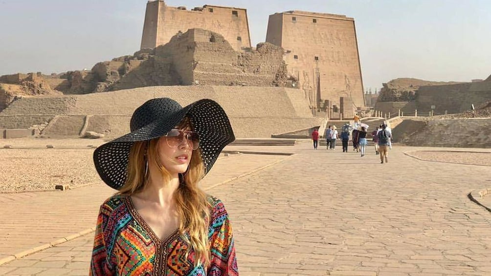 Woman in large hat poses with the Temple of Horus at Edfu in the background