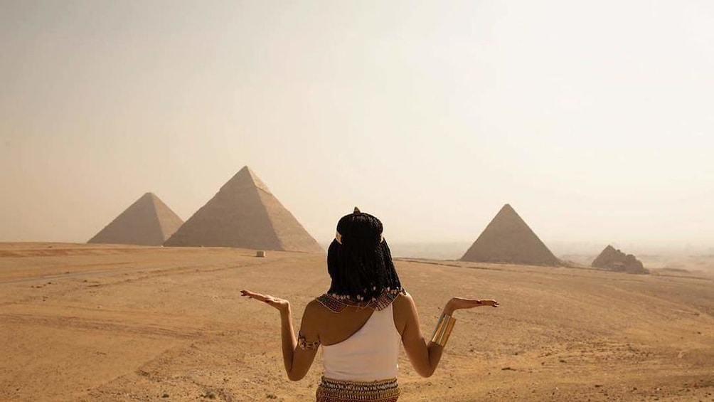 Woman poses with hats flat and raised to facing the Pyramids of Giza