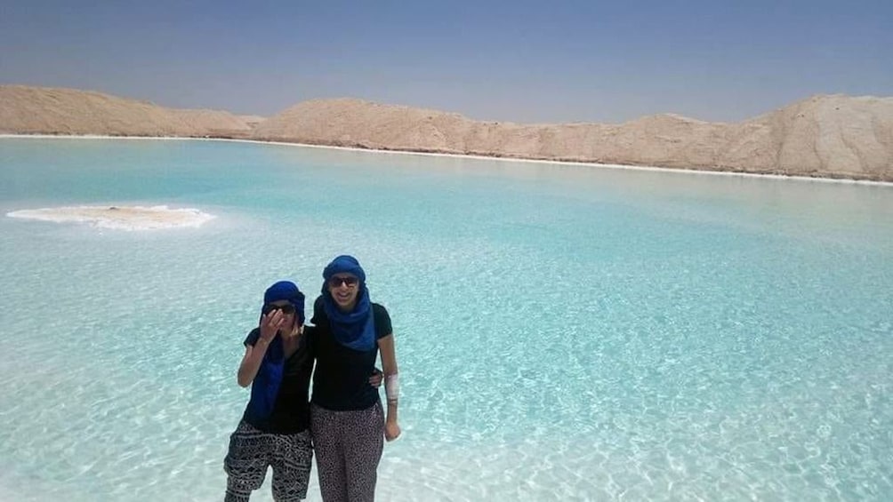 Two women pose in front of large, light blue oasis in Egypt