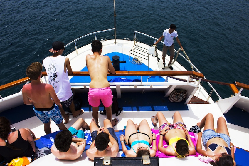 Tourists sunbathe and stand on the back of sailboat near Comino Island