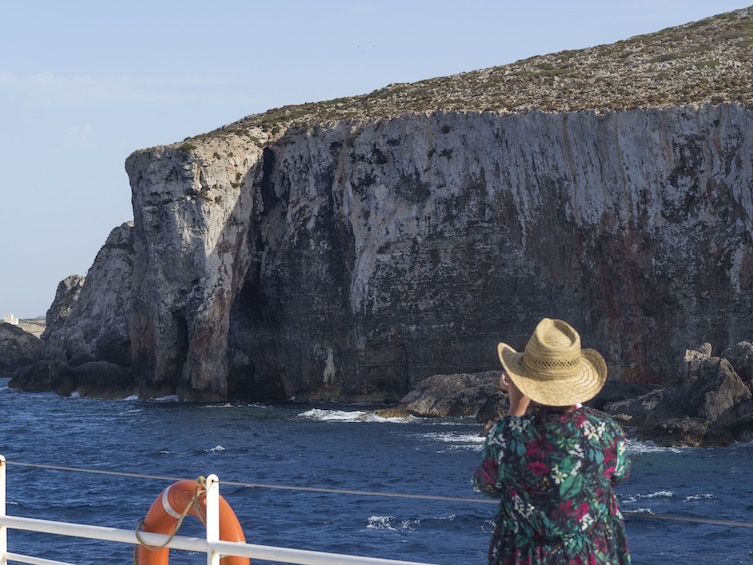 Man in hat looks out towards Comino Island from boat