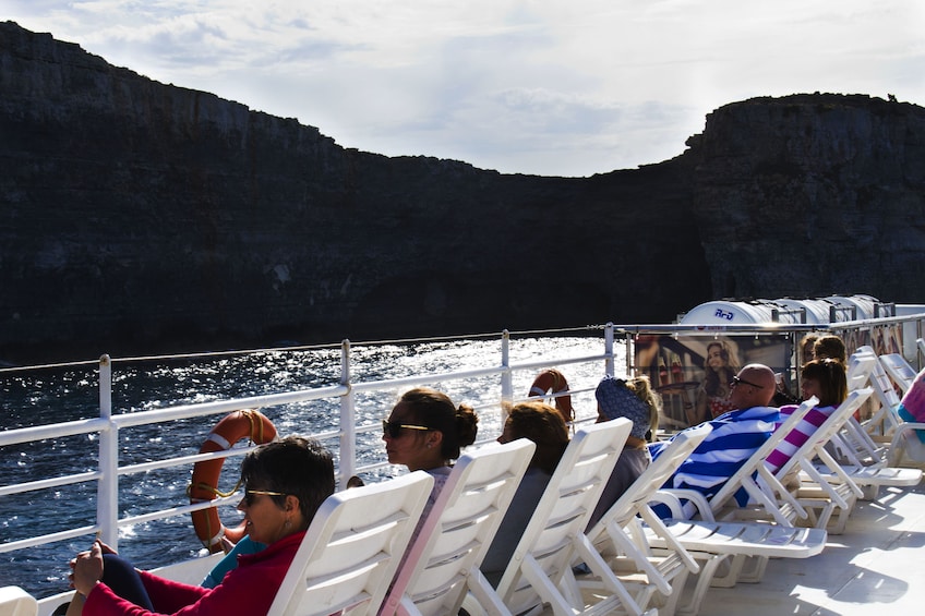 Tourists sit on lounge chairs on deck of cruise ship in Malta