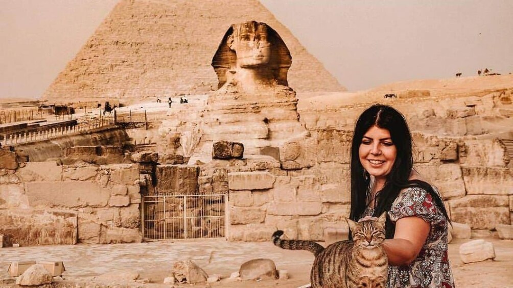 Woman pets cat in front of Sphinx and Pyramids of Giza