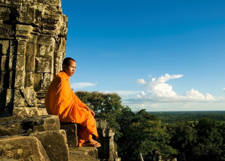 Monk in orange robe sits on stone at Angkor Wat Temple