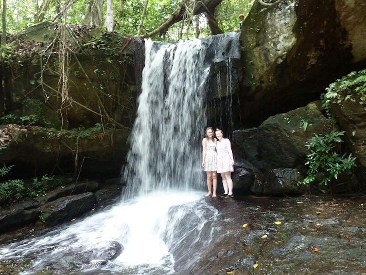 Two girls pose next to waterfall at Kbal Spean in Siem Reap, Cambodia